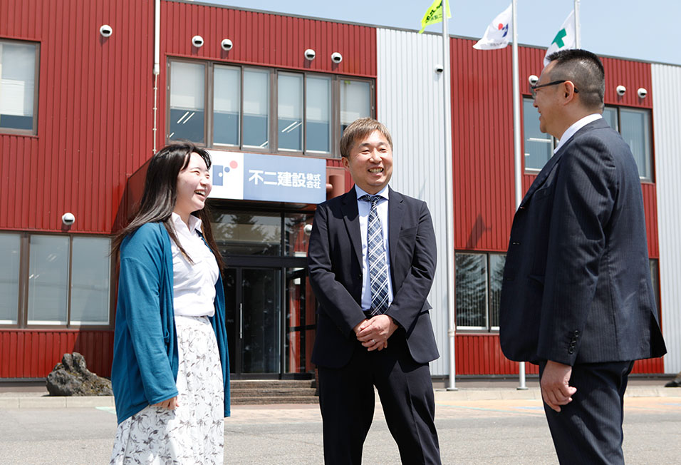 不二建設の社屋前で笑顔の職員たち