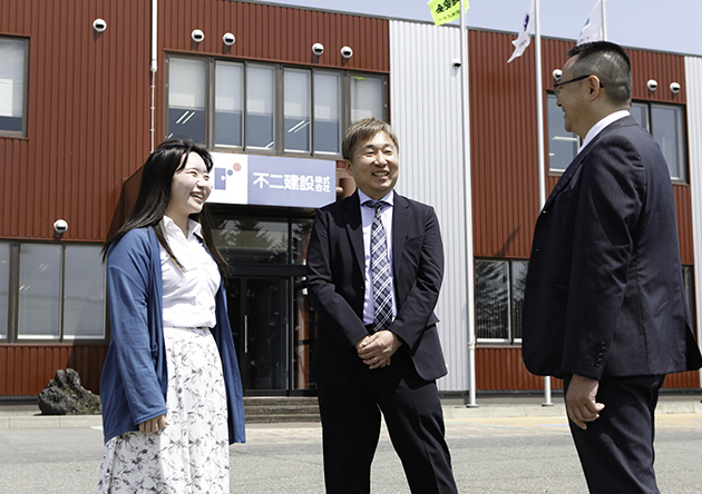 不二建設の社屋前で笑顔の職員たち